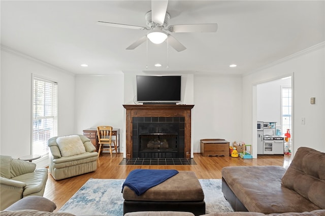 living room featuring ornamental molding, hardwood / wood-style floors, a tile fireplace, and ceiling fan