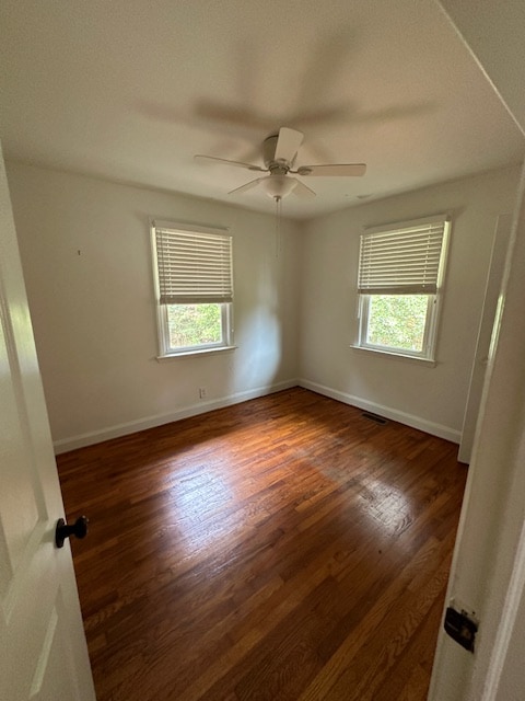 spare room featuring wood walls, dark wood-type flooring, and ceiling fan