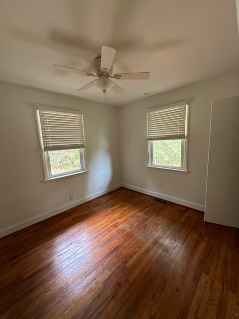 spare room featuring dark wood-type flooring, plenty of natural light, and ceiling fan