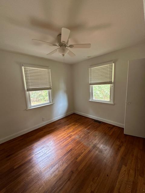 empty room featuring a wealth of natural light, dark hardwood / wood-style floors, and ceiling fan