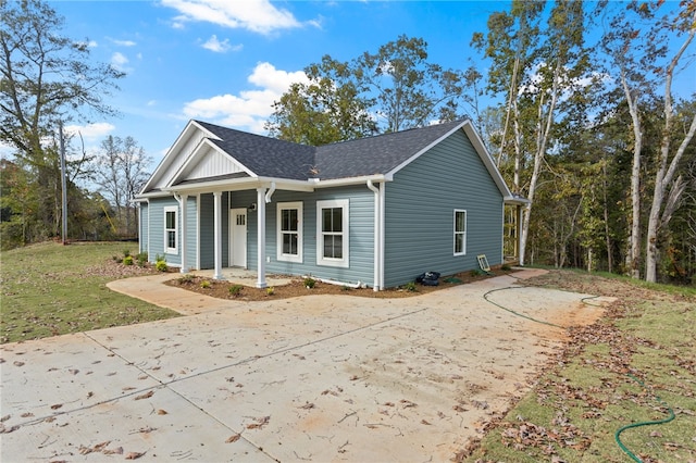 view of front facade featuring driveway, covered porch, a shingled roof, and a front lawn