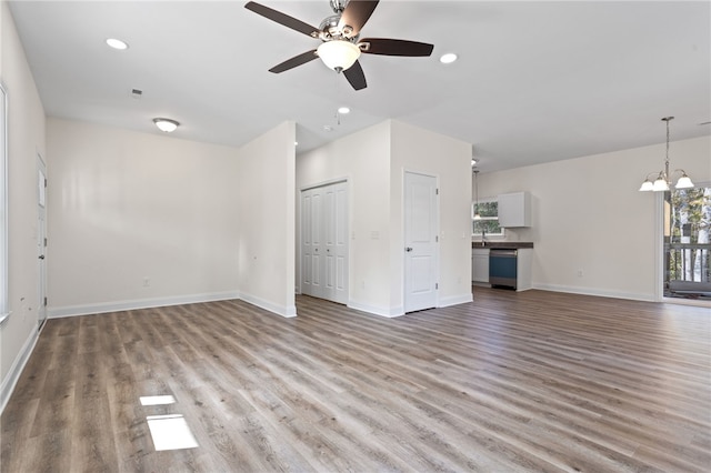 unfurnished living room with ceiling fan with notable chandelier, recessed lighting, baseboards, and wood finished floors