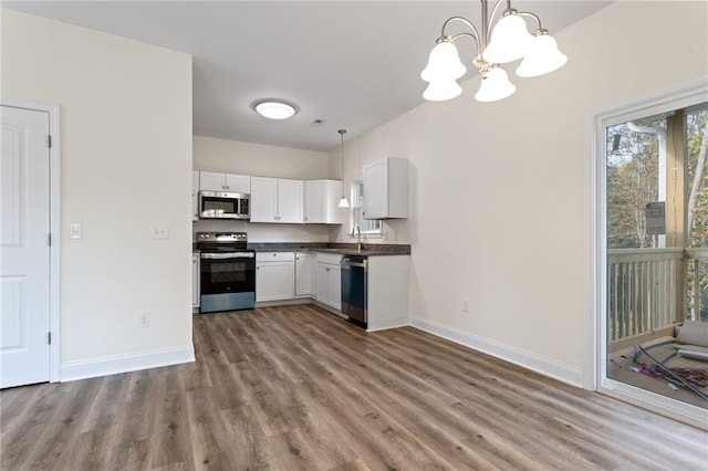 kitchen with wood finished floors, white cabinetry, baseboards, appliances with stainless steel finishes, and dark countertops