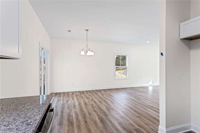 unfurnished dining area featuring an inviting chandelier, visible vents, baseboards, and wood finished floors