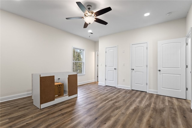 unfurnished bedroom with dark wood-style floors, ceiling fan, baseboards, and multiple closets