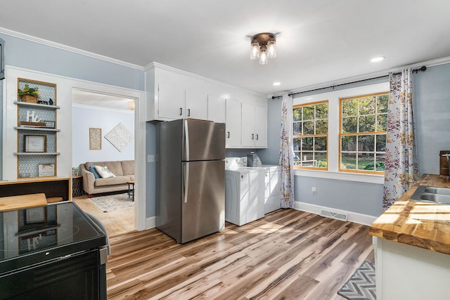 kitchen featuring butcher block counters, black range with electric cooktop, stainless steel fridge, white cabinets, and washing machine and clothes dryer