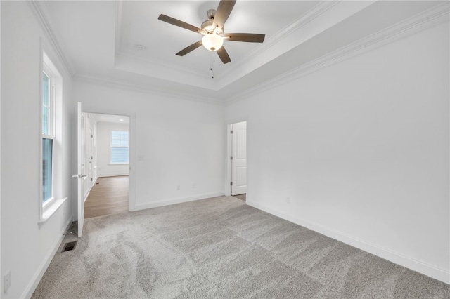 empty room with a raised ceiling, ornamental molding, and light colored carpet