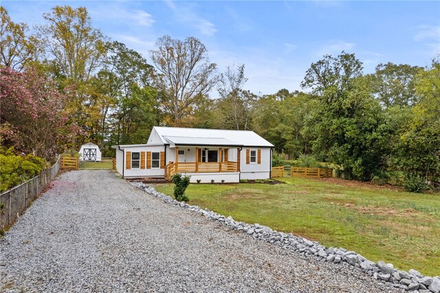 view of front of home featuring a front yard, fence, gravel driveway, covered porch, and an outdoor structure