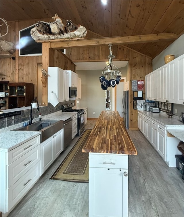 kitchen with stainless steel appliances, light hardwood / wood-style flooring, white cabinets, wooden walls, and butcher block countertops