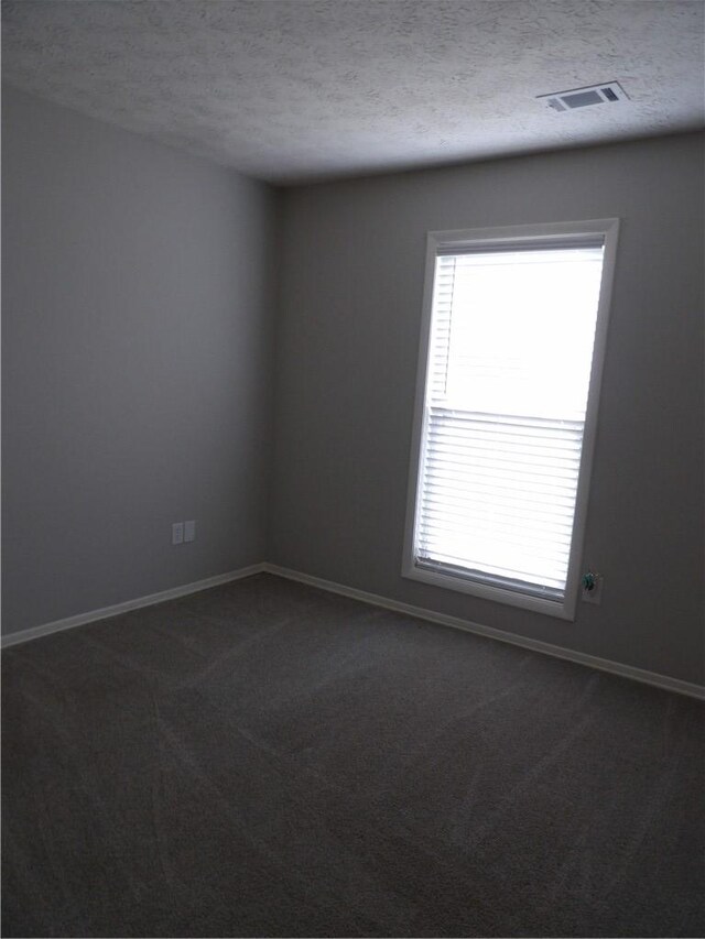 unfurnished room featuring plenty of natural light, dark colored carpet, a textured ceiling, and baseboards