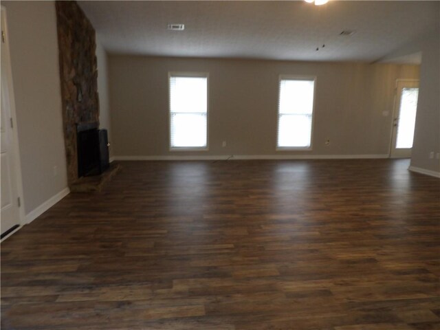 unfurnished living room featuring a large fireplace, dark wood finished floors, and baseboards