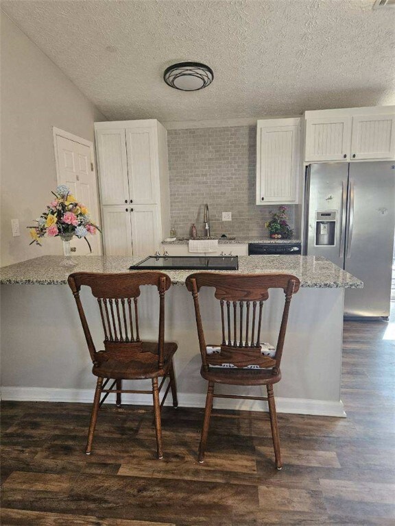 kitchen with stainless steel refrigerator with ice dispenser, dark wood-style floors, a breakfast bar, white cabinets, and a textured ceiling
