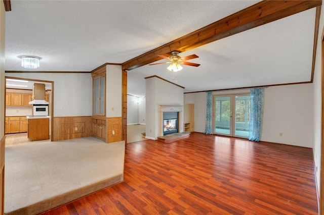 unfurnished living room featuring a textured ceiling, a wainscoted wall, light wood-style floors, a glass covered fireplace, and crown molding