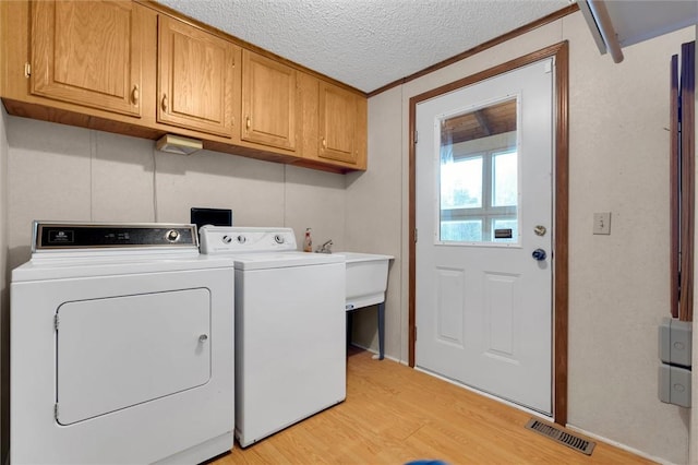 laundry area featuring cabinets, light hardwood / wood-style floors, a textured ceiling, washer and clothes dryer, and ornamental molding