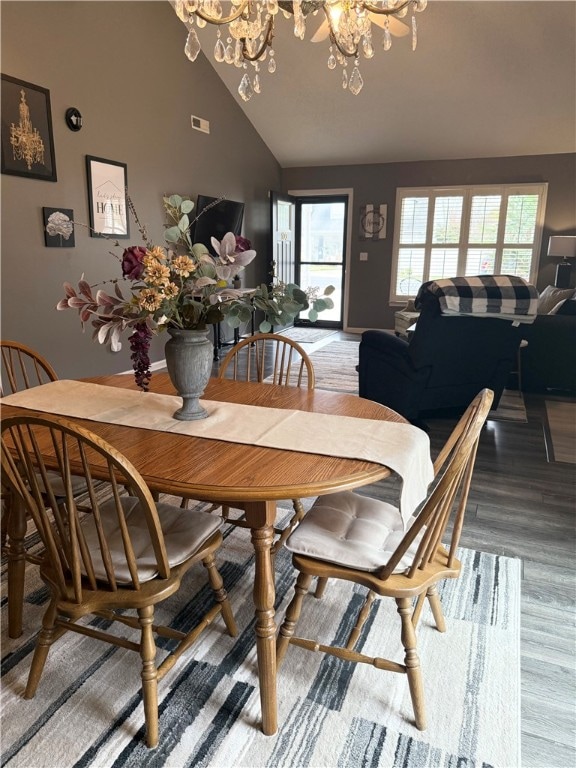 dining space featuring high vaulted ceiling, a wealth of natural light, wood-type flooring, and a chandelier