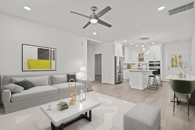 living room featuring ceiling fan, sink, and light hardwood / wood-style flooring