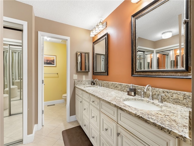 bathroom featuring toilet, vanity, a textured ceiling, and tile patterned floors