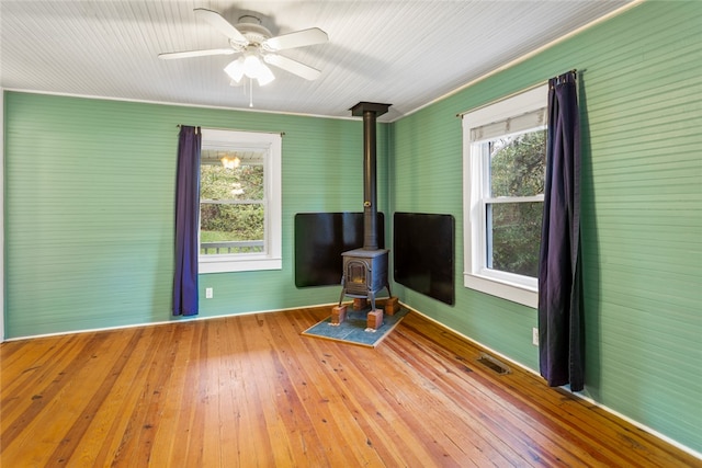 unfurnished room featuring hardwood / wood-style floors, a wood stove, plenty of natural light, and ceiling fan