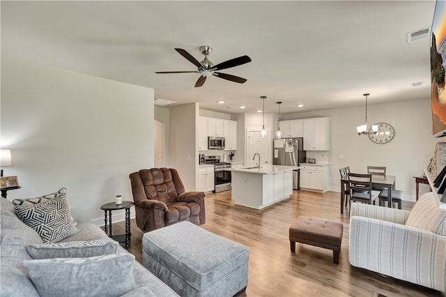 living room featuring a fireplace, light hardwood / wood-style floors, ceiling fan with notable chandelier, and sink