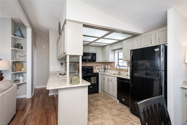 kitchen featuring black appliances, light stone countertops, sink, decorative backsplash, and hardwood / wood-style flooring