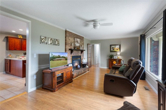 living room featuring ceiling fan, a fireplace, crown molding, and light wood-type flooring