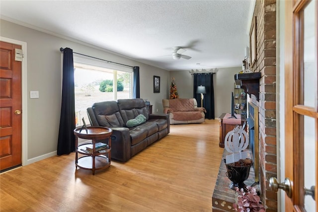 living room featuring ceiling fan, light wood-type flooring, a textured ceiling, and a brick fireplace