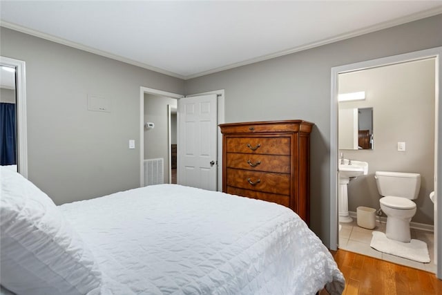 bedroom featuring ensuite bathroom, light hardwood / wood-style flooring, and ornamental molding