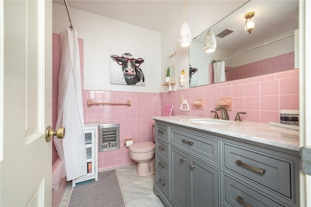 bathroom with heating unit, vanity, tile walls, and toilet