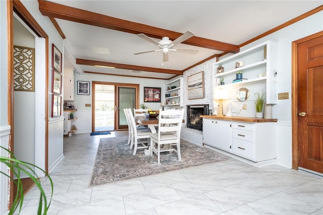 dining area with built in shelves, crown molding, a large fireplace, beamed ceiling, and ceiling fan