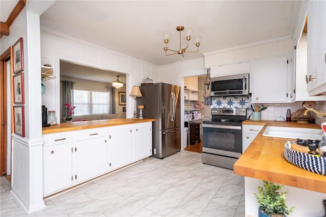 kitchen featuring stainless steel appliances, white cabinets, backsplash, and decorative light fixtures