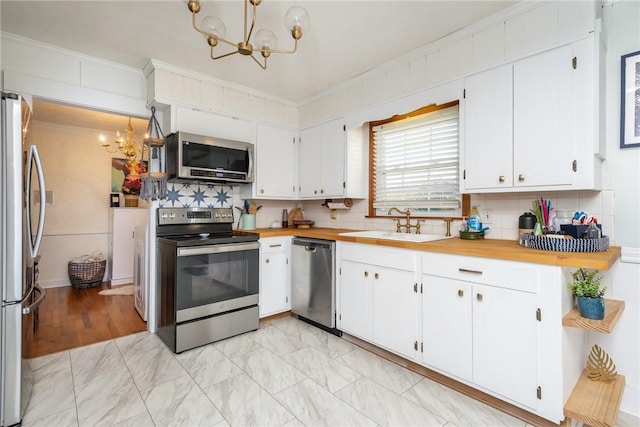 kitchen featuring sink, an inviting chandelier, ornamental molding, appliances with stainless steel finishes, and white cabinets