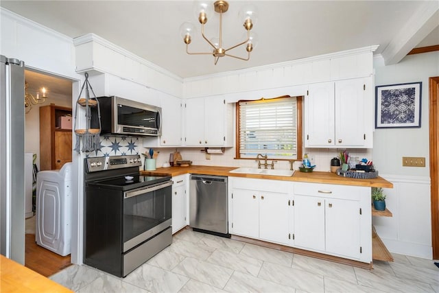 kitchen with appliances with stainless steel finishes, washer / clothes dryer, white cabinetry, sink, and wooden counters