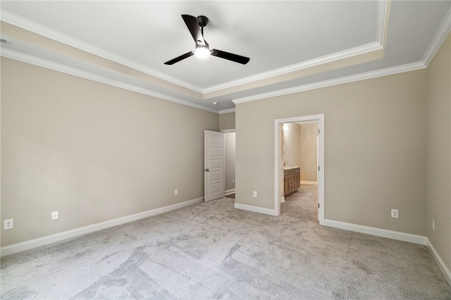 unfurnished bedroom featuring ensuite bath, light carpet, ceiling fan, crown molding, and a tray ceiling