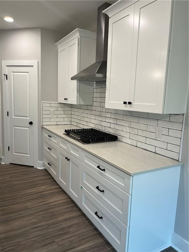 kitchen with dark wood-type flooring, wall chimney exhaust hood, stainless steel gas cooktop, light stone countertops, and white cabinets