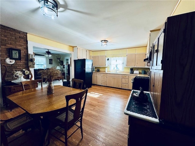 kitchen featuring brick wall, black refrigerator, range, light brown cabinets, and light wood-type flooring