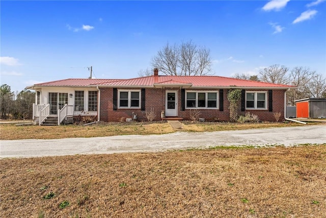 single story home featuring metal roof, a front lawn, and brick siding