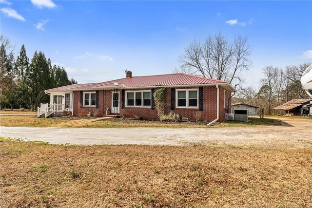 single story home with metal roof, a chimney, a front lawn, and brick siding