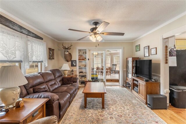 living room featuring a textured ceiling, ceiling fan, light wood-type flooring, and crown molding