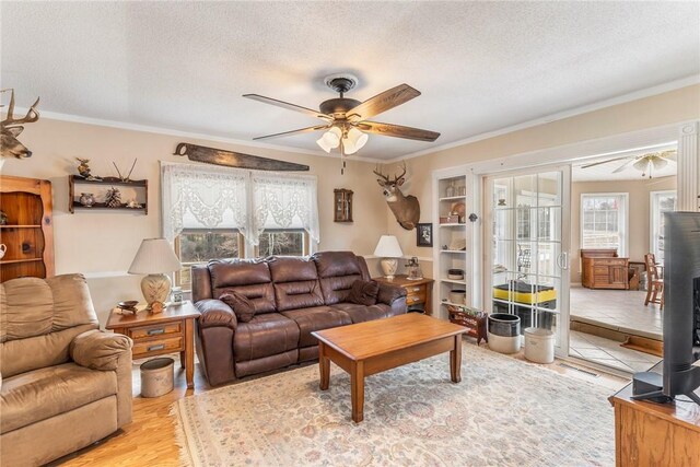 living room featuring a textured ceiling, ceiling fan, ornamental molding, and light wood finished floors