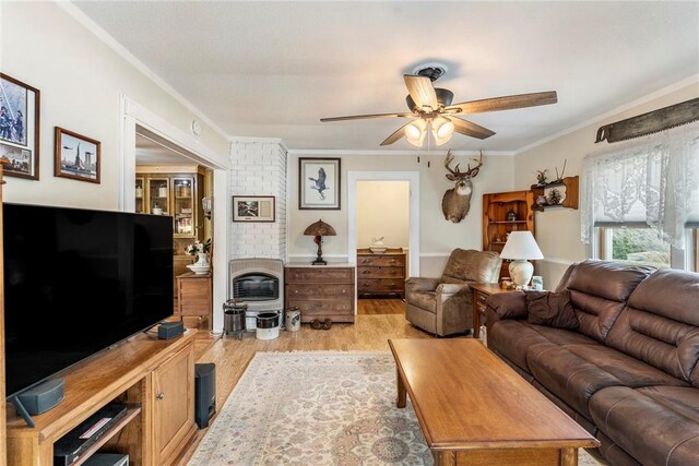 living area featuring ceiling fan, a fireplace, light wood-style flooring, and crown molding