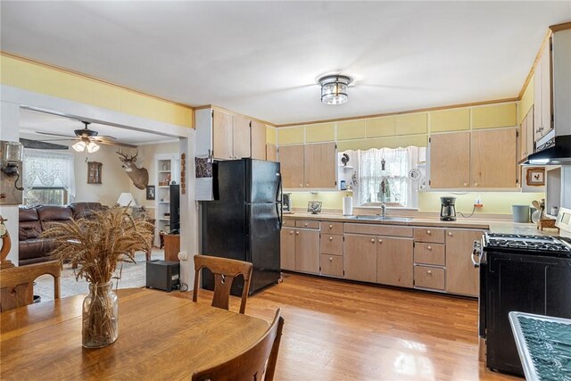 kitchen featuring light countertops, light wood-style floors, a sink, under cabinet range hood, and black appliances