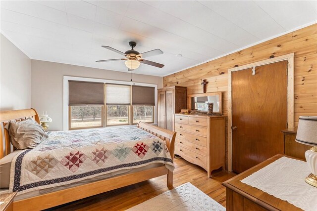 bedroom with light wood-type flooring, ceiling fan, and wooden walls