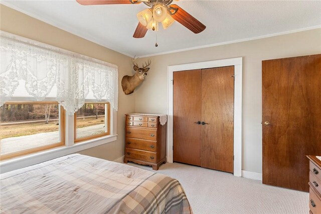 bedroom with light colored carpet, a ceiling fan, baseboards, a closet, and crown molding