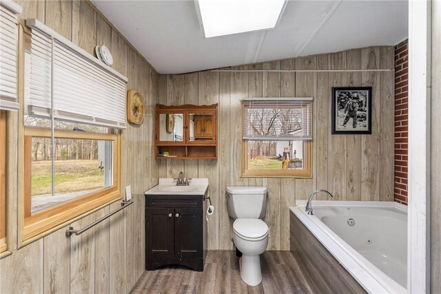 full bathroom with toilet, wood finished floors, a whirlpool tub, vanity, and wood walls