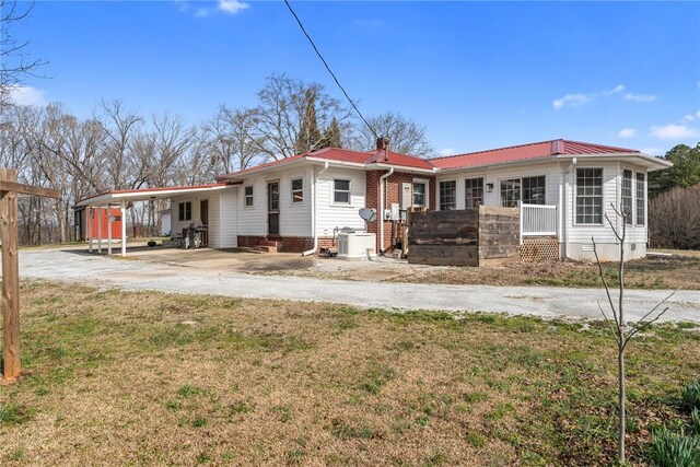 rear view of house featuring a yard, concrete driveway, entry steps, metal roof, and an attached carport