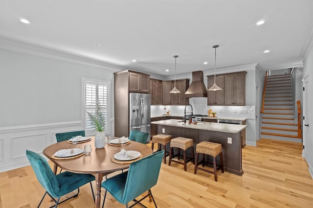 kitchen featuring a center island with sink, decorative light fixtures, stainless steel fridge, and light hardwood / wood-style floors