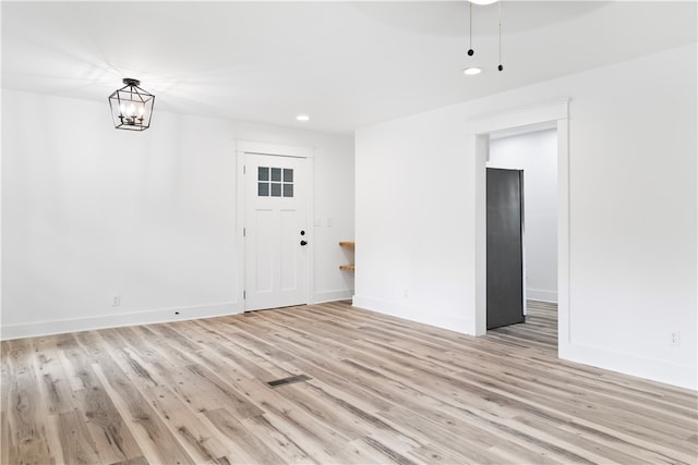 spare room featuring an inviting chandelier and light hardwood / wood-style flooring