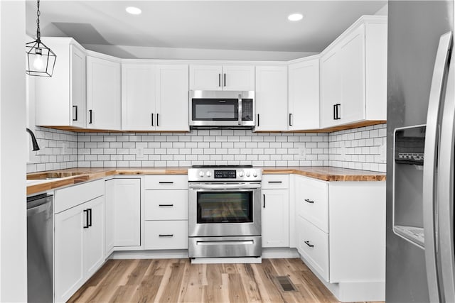 kitchen with wood counters, light wood-type flooring, appliances with stainless steel finishes, decorative light fixtures, and white cabinetry