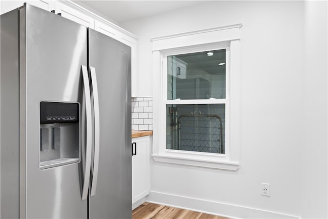 kitchen featuring white cabinetry, stainless steel fridge with ice dispenser, butcher block countertops, decorative backsplash, and light wood-type flooring