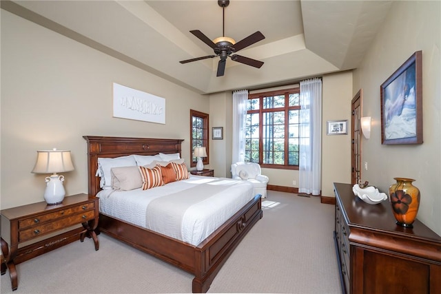 bedroom featuring a raised ceiling, ceiling fan, and light colored carpet